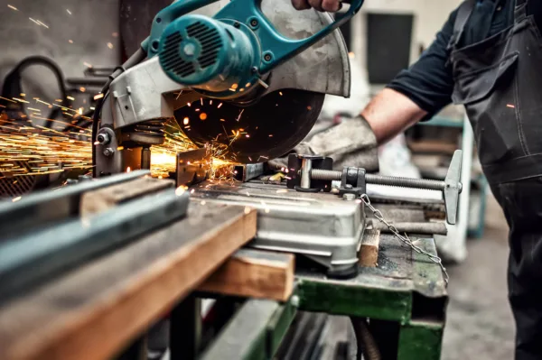 Arbeiter schneidet Metall mit einer Gehrungsbandsäge, während Funken sprühen.