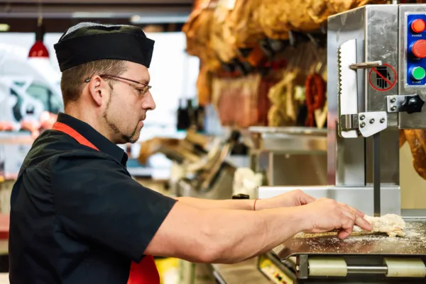 Ein Metzger, der mit einer Tischbandsäge arbeitet, um Fleisch oder Knochen zu schneiden.