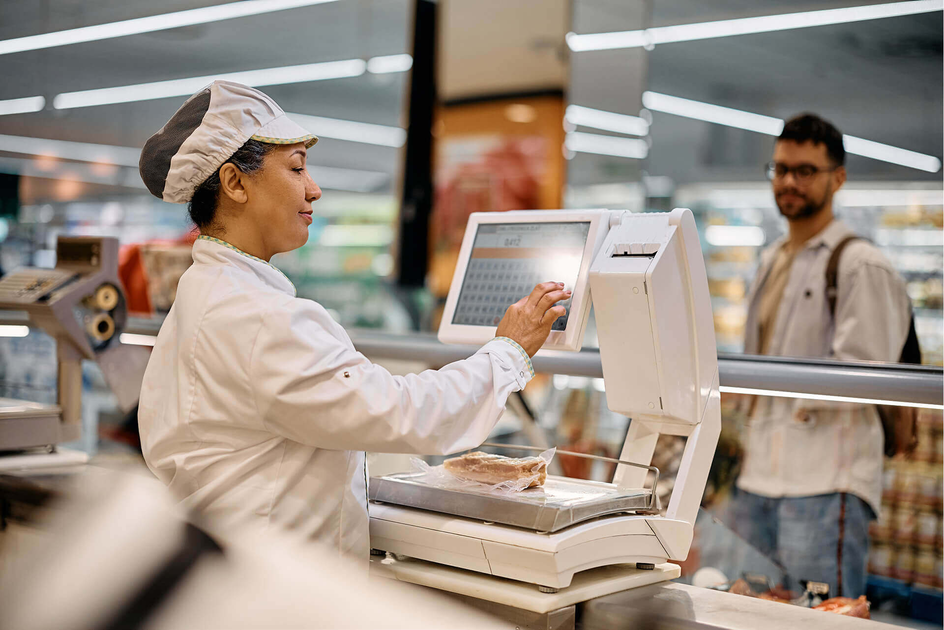 Metzgereimitarbeiterin bedient eine digitale Ladenwaage mit Touchscreen und wiegt ein vakuumiertes Stück Fleisch. Symbolbild - wir verkaufen Waagen von Dibal, Soehnle, Adams