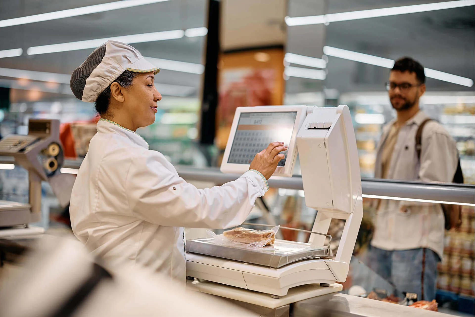 Metzgereimitarbeiterin bedient eine digitale Ladenwaage mit Touchscreen und wiegt ein vakuumiertes Stück Fleisch. Symbolbild - wir verkaufen Waagen von Dibal, Soehnle, Adams