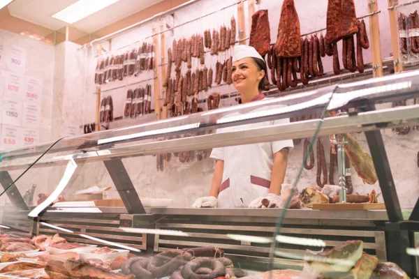 Freundliche Metzgereimitarbeiterin hinter einer Fleisch- und Wursttheke mit einer Auswahl an Wurstwaren und Fleischprodukten.