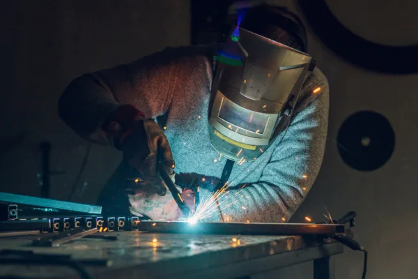 Schweisser bei der Arbeit mit Schutzmaske und Handschuhen, um Metallteile präzise zu verbinden.